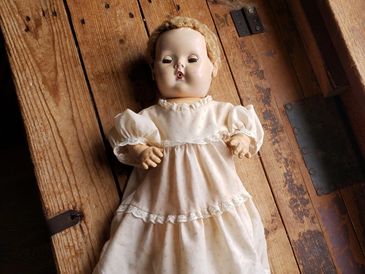Vintage doll in a white dress on a wooden surface.