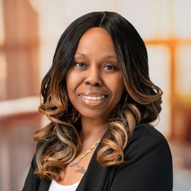 Confident woman with curled hair and a black blazer smiling with arms crossed.