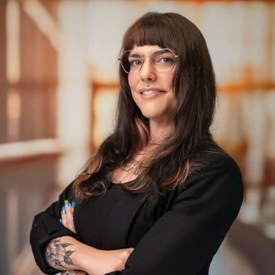 Confident woman with glasses and tattoos smiles with arms crossed.