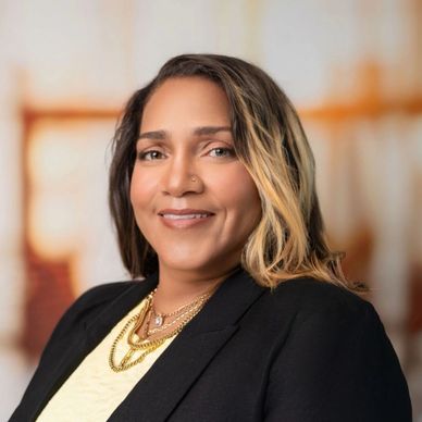 Professional woman in a black blazer and yellow top smiling confidently.