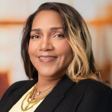 Professional woman in a black blazer and yellow top smiling confidently.