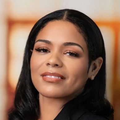 Professional woman in black blazer and pink top posing confidently.