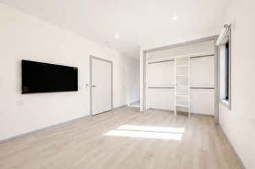 Empty modern room with light wood flooring and wall-mounted TV.