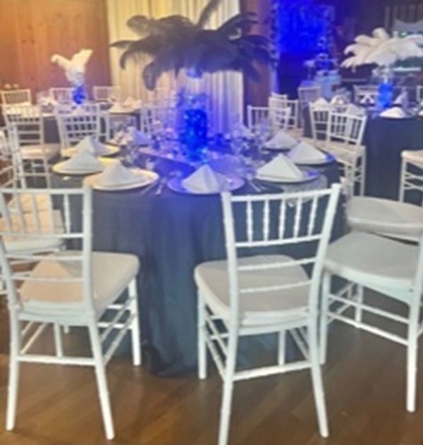 Elegant dining setup with white chairs and feather centerpieces.