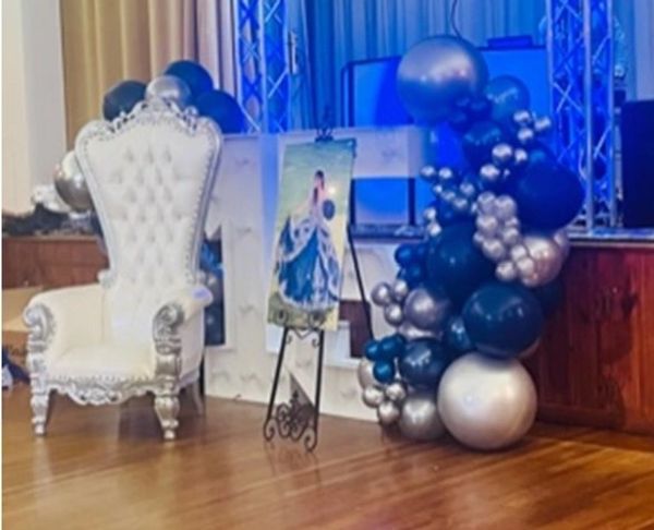 Elegant white throne chair with blue and silver balloon decor beside a picture on an easel.