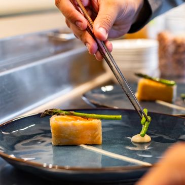 Plating gourmet dish with asparagus and sauce.