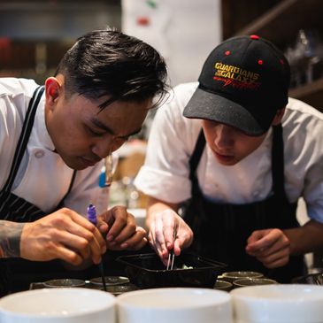 Two chefs meticulously plating a dish in a professional kitchen.