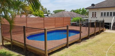 Backyard swimming pool surrounded by a wooden deck and safety fence.