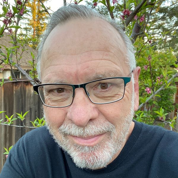 Smiling older man with glasses in a garden setting.