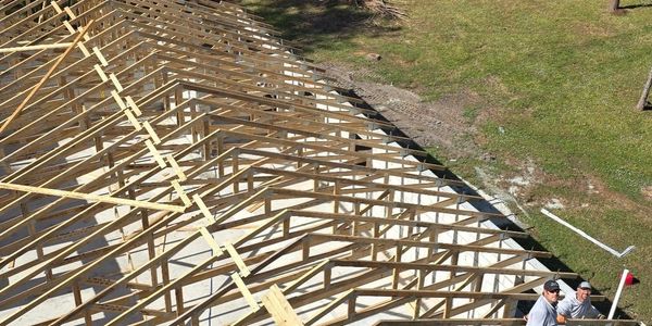 Wooden roof trusses being installed on a building frame outdoors.