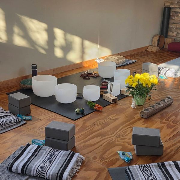 A serene meditation space with singing bowls, cushions, and yellow flowers.