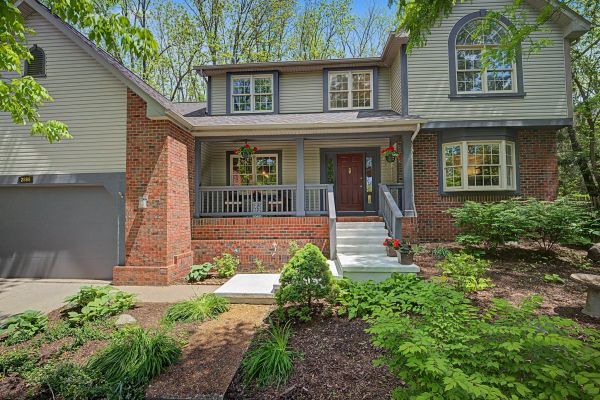 Two-story house with brick and gray siding, a porch, and a well-maintained garden.