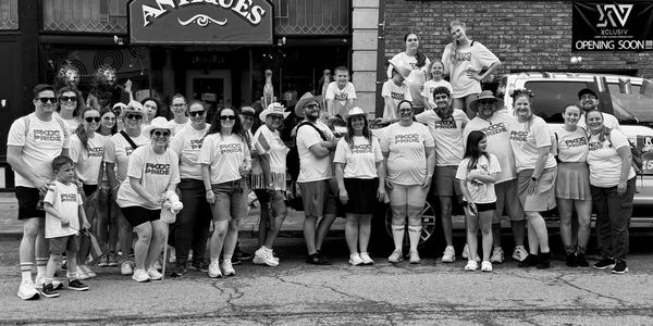 Group of people wearing matching PKDC Pride shirts posing outside an antique store.