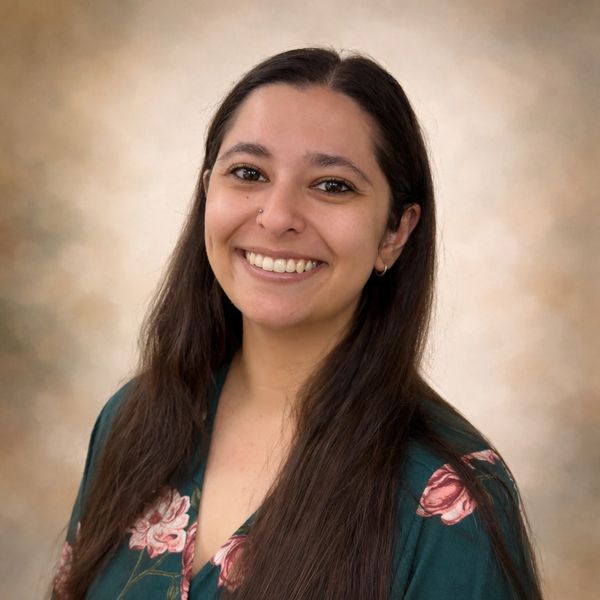 Smiling woman with long dark hair and floral top against a soft background.