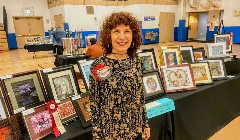 Woman stands proudly by her award-winning artwork at a local exhibition.