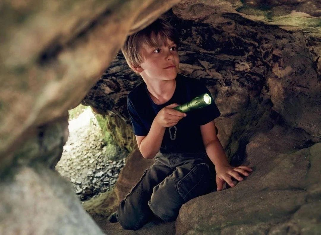 A boy explores a cave with a flashlight, looking curious and cautious.