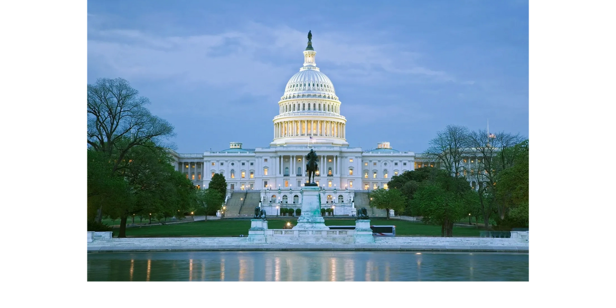 The illuminated U.S. Capitol building at dusk with a statue in the foreground.