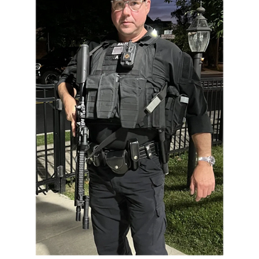 A security officer in tactical gear holding a rifle at night.