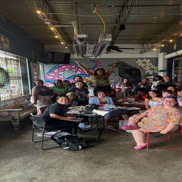 Group of people gathered inside a colorful cafe with mural art.