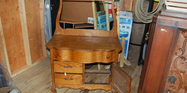 Antique wooden vanity with drawers and a mirror in a storage room.