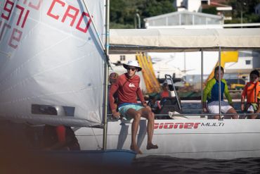 Sailors prepare a small sailboat on calm waters near a dock.
