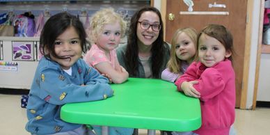 Toddler teacher at table with children.