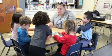 Teacher at table while children work on puzzles.