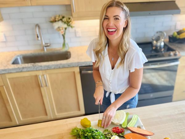 A smiling woman chopping vegetables in a bright kitchen.