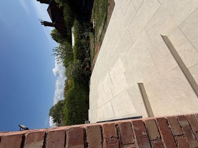 Newly paved beige stone patio with steps in a backyard garden under clear blue sky.