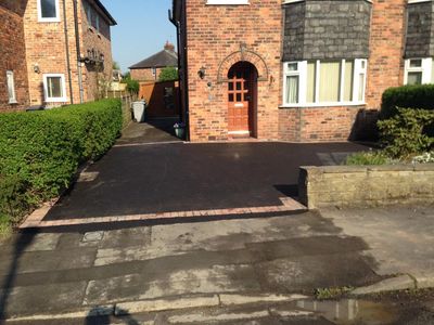 Newly paved driveway in front of a brick house with greenery on the sides.