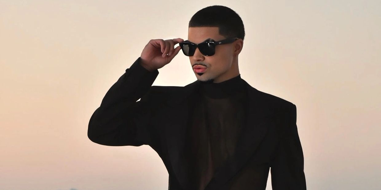 Man in black blazer and sunglasses striking a confident pose.