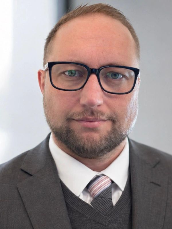 Professional man in glasses and suit with a subtle smile.
