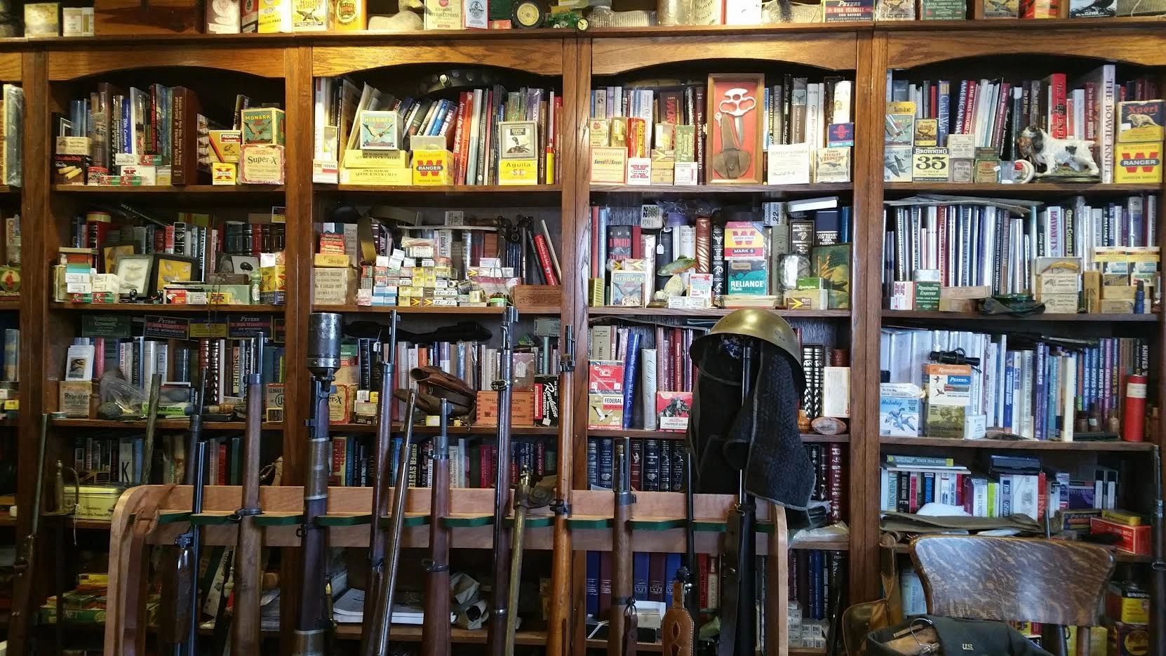 A wooden shelf filled with books, ammunition, and old rifles.