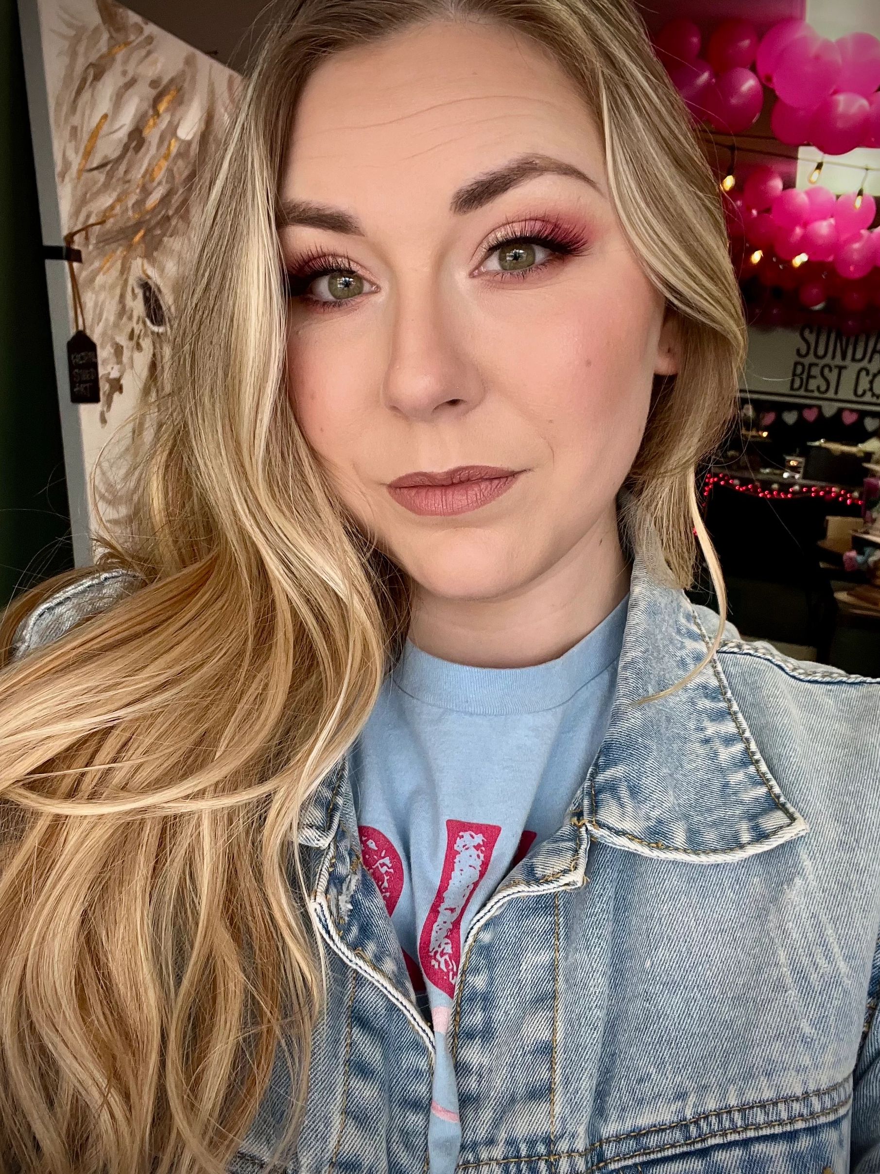 Close-up of a woman with blonde hair and pink eyeshadow wearing a denim jacket.