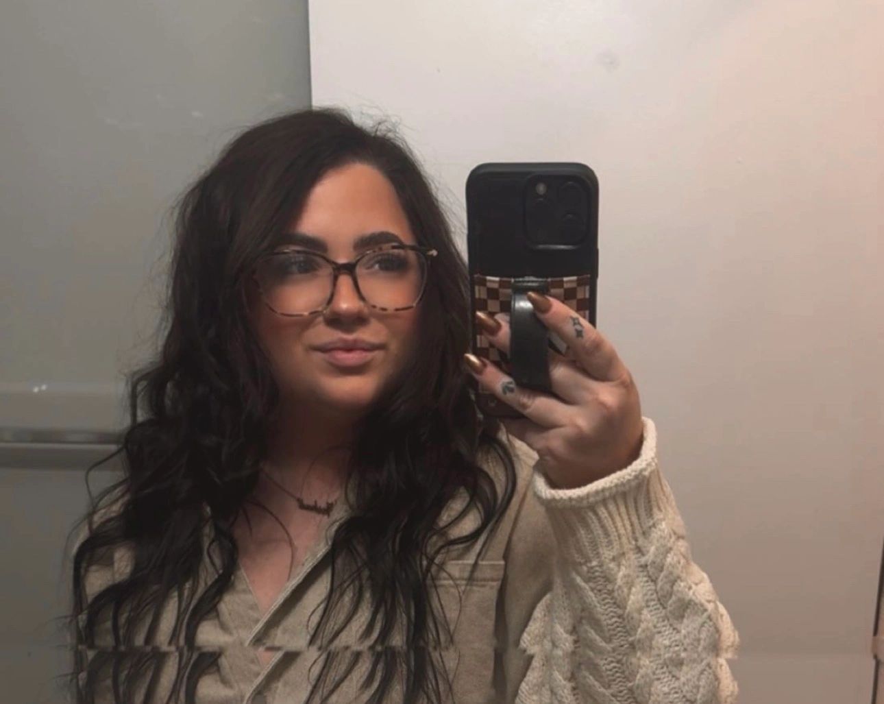 Woman with long dark hair and glasses takes a mirror selfie.
