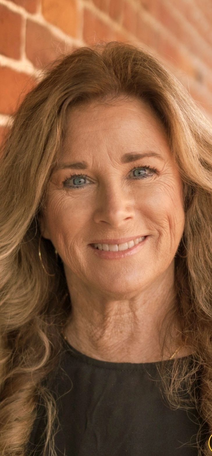 Smiling middle-aged woman with wavy hair against a brick wall.