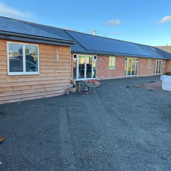 A courtyard with gravel ground, a wheelbarrow of bricks, and solar panels on the roof.