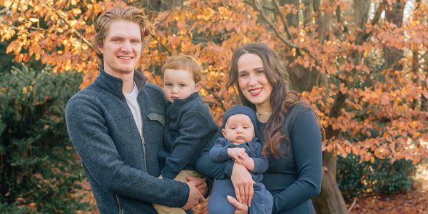 Happy family of four posing outdoors in autumn with colorful leaves.