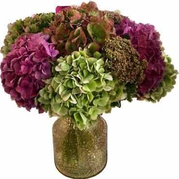 A bouquet of green and purple hydrangeas in a textured glass vase.