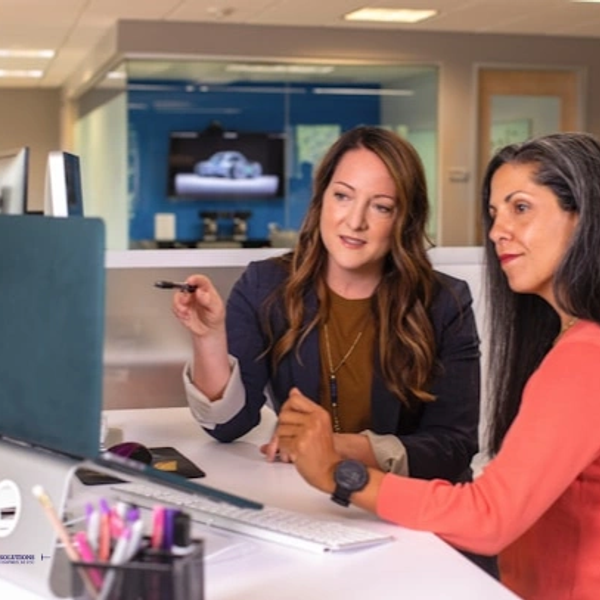 Two women collaborating at a computer in an office setting.