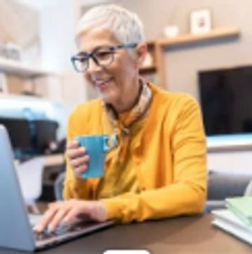 woman at computer holding coffee smiling at what she is reading.