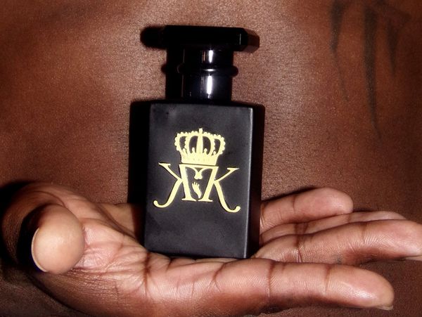 Black perfume bottle with gold crown logo held in a person's hand.