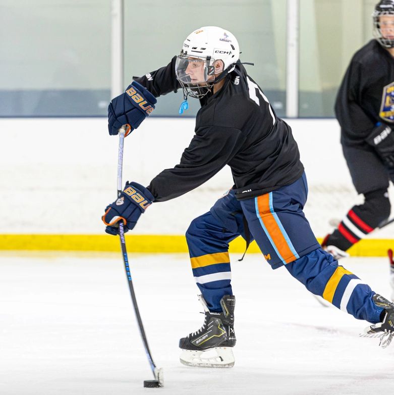 Hockey player in black jersey about to hit the puck.