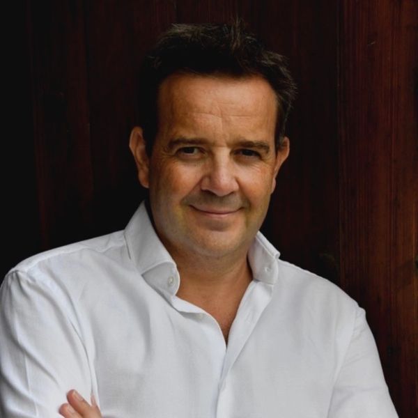 Man in white shirt smiling with arms crossed against a dark wooden background.