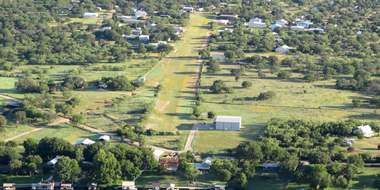A small rural airstrip surrounded by houses and greenery.