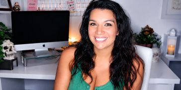 Smiling woman with curly hair wearing a green top in a cozy room.