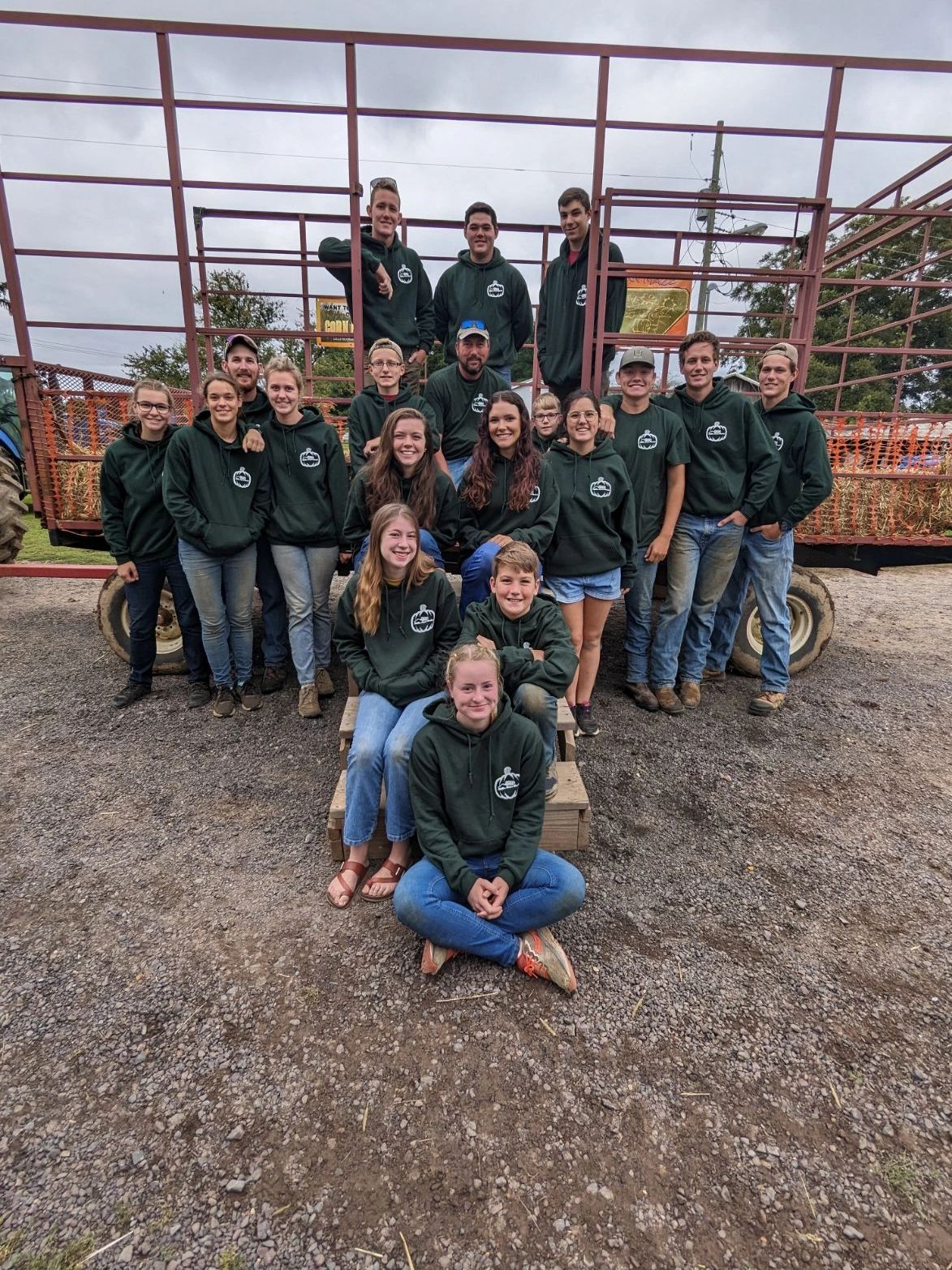 Group of people in matching hoodies posing outdoors by a wagon.