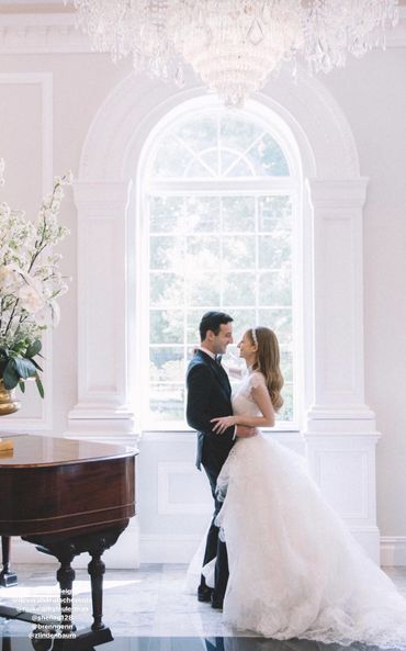 Bride and groom embracing in a bright, elegant room with a grand piano.