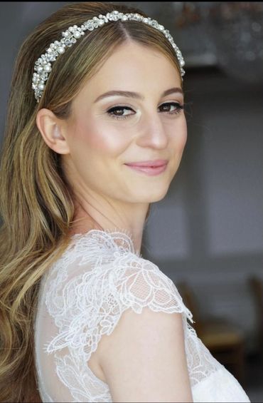 Bride with pearl headband and lace dress smiling softly.