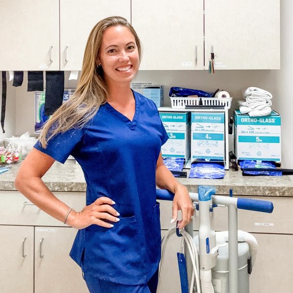 Smiling healthcare professional in blue scrubs standing in a medical room.